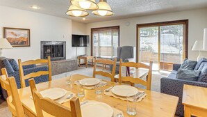 A dining area with a wooden table set for four, surrounded by chairs, with a fireplace and television in the background. - Walk to Hideaway Park! All-season Winter Park Gem (Winter Park)