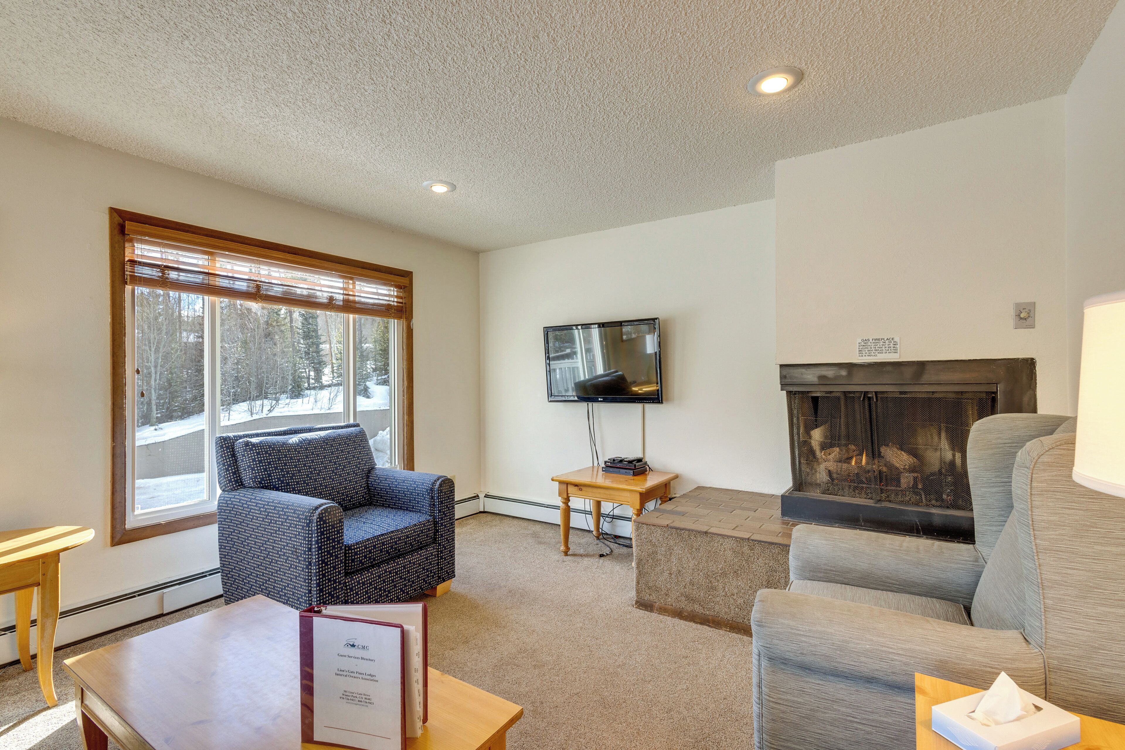 A living room with a fireplace, a television mounted on the wall, and a window with blinds.
