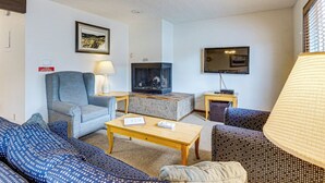 Ein Wohnzimmer mit Sofa, Sessel, Couchtisch, Kamin, Fernseher und Lampe.