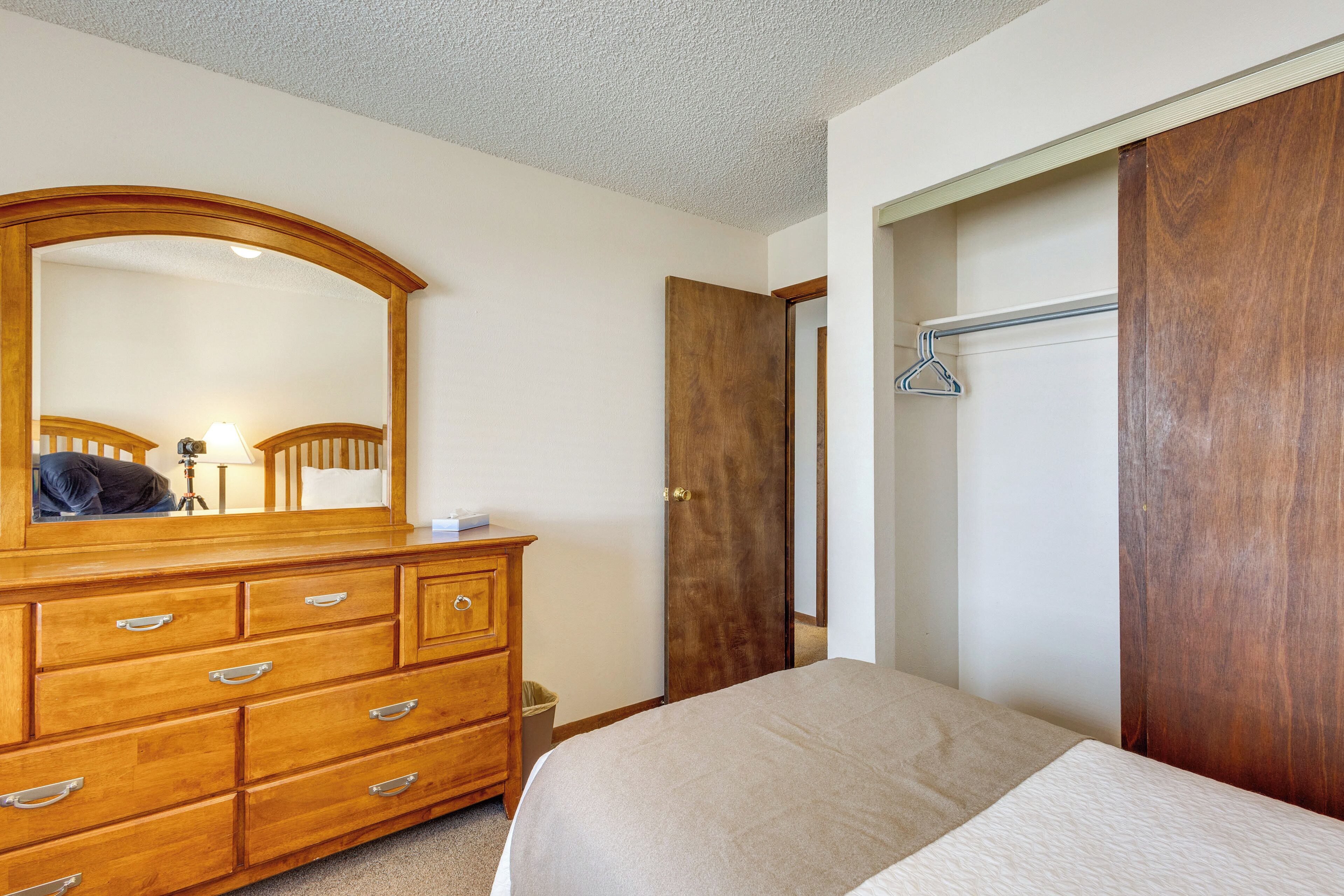 Une chambre avec une commode en bois, un lit, un miroir, une armoire et un portant à vêtements.