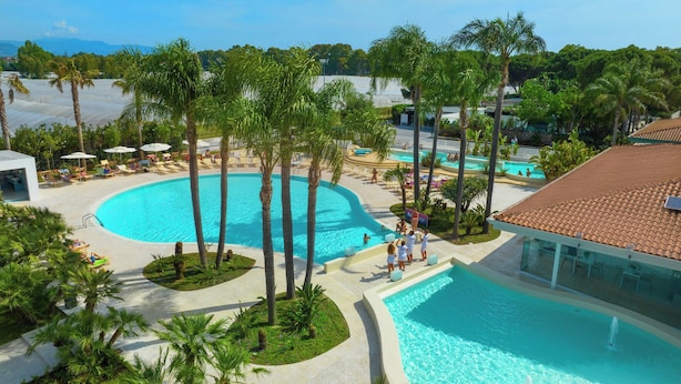 Een resort met meerdere zwembaden, palmbomen en uitzicht op de bergen.