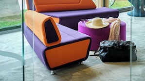 Een moderne zithoek met een paars-oranje bank, een klein rond tafeltje en een zwarte handtas.