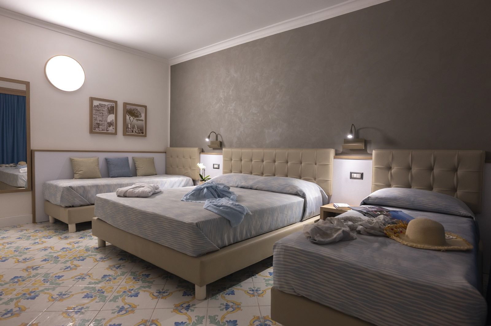 Une chambre d’hôtel avec deux lits, un miroir rond, des œuvres d’art accrochées au mur et un sol à motifs.