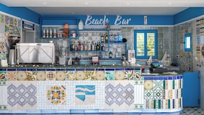 Een bar met een blauw-wit betegelde achterwand, een toonbank met diverse flessen en een bord waarop staat 'Beach Bar'.