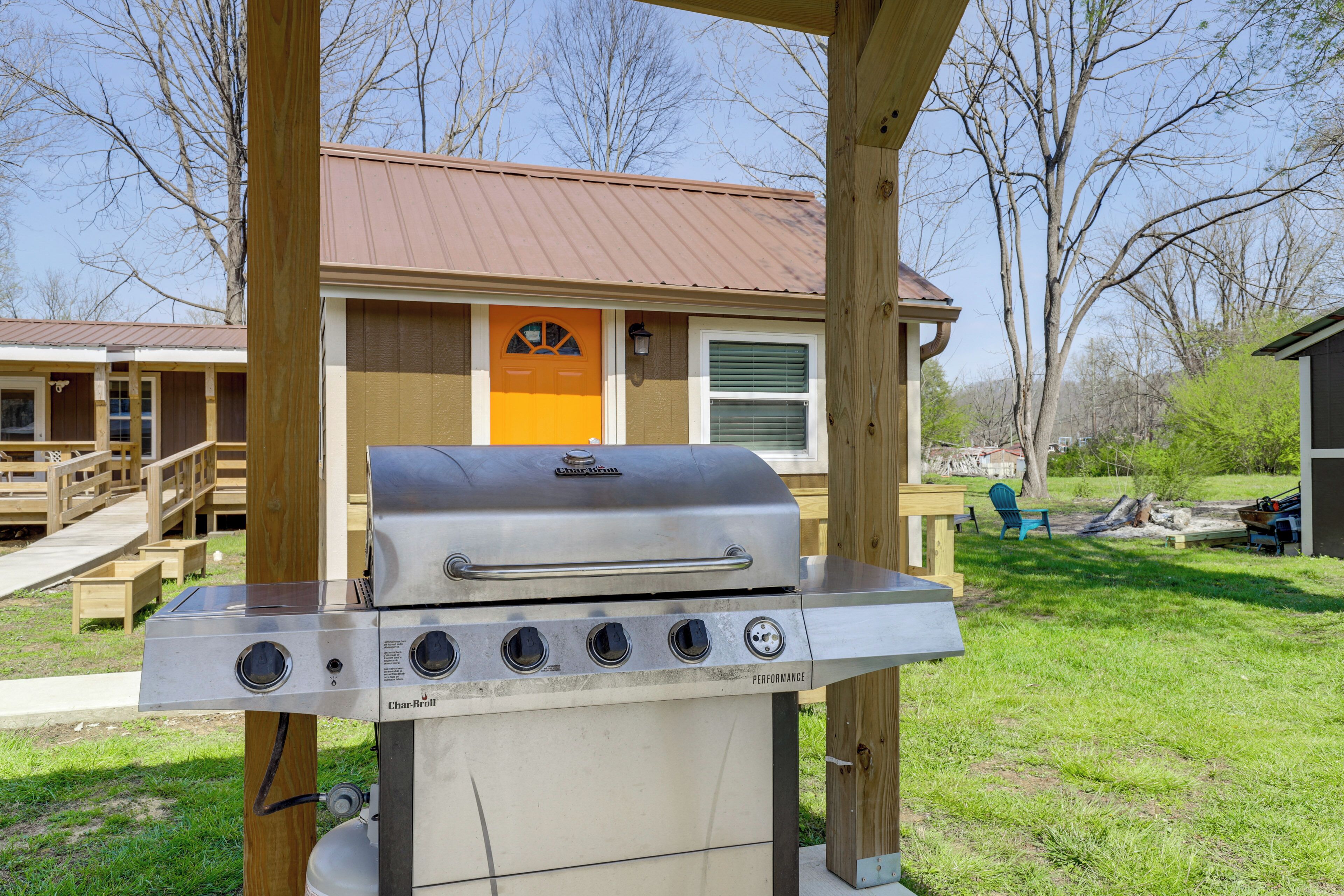 Ein Grill im Garten mit einer Holzterrasse, einem kleinen Gebäude mit brauner Tür und blauem Himmel.