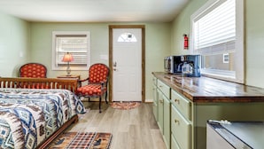 A room with a bed, two chairs, a small table with a lamp, a kitchenette, and a door with a window. - 2 Mi to Great Smoky Mtns NP! Cozy Cabin Retreat (Townsend)