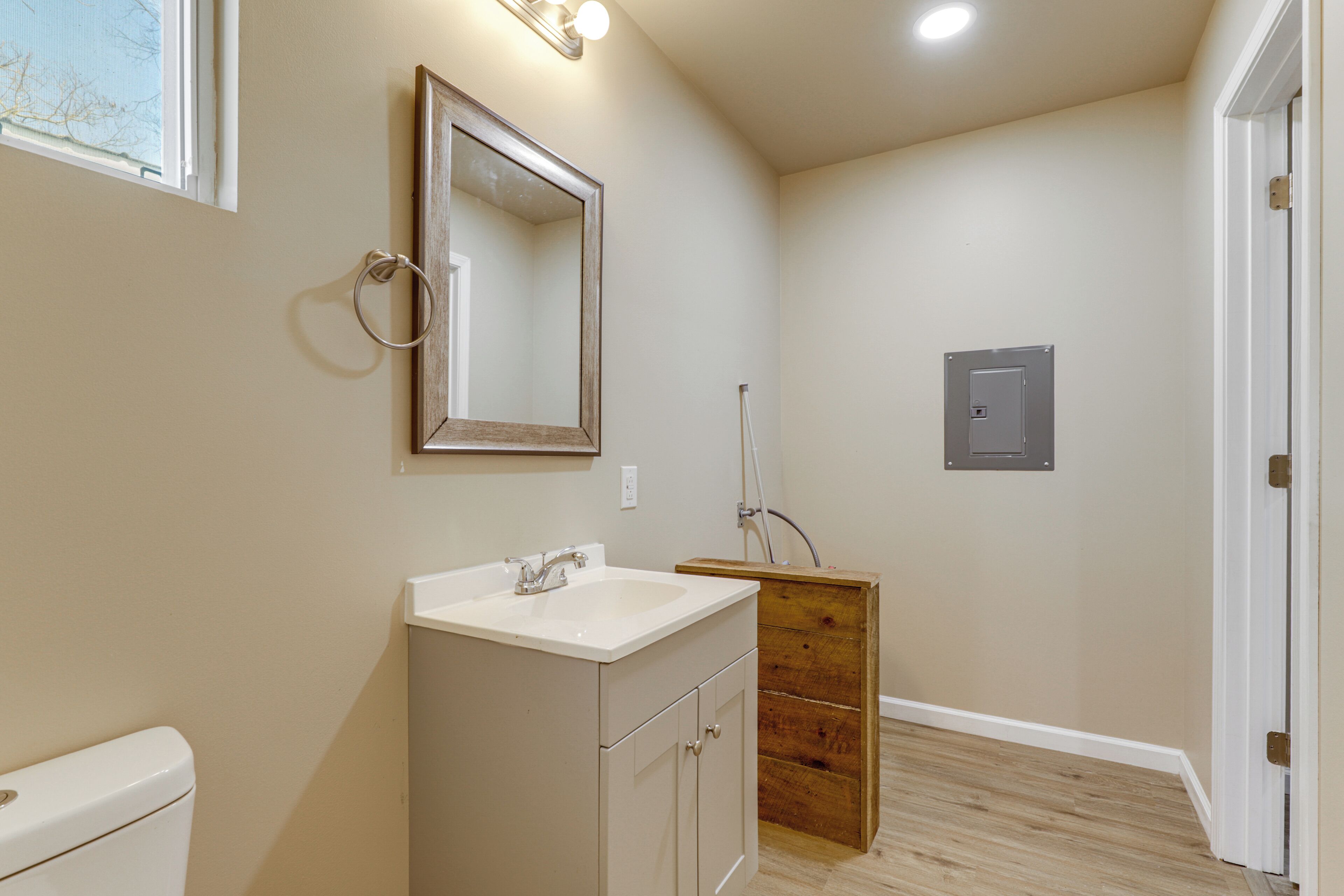 A bathroom with a toilet, sink, mirror, wooden cabinet, and a light switch on the wall.