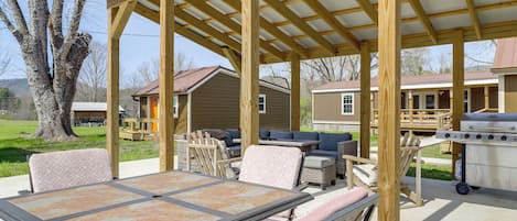 A covered outdoor patio with a table and chairs, a grill, and a wooden deck.