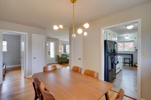 Ein Essbereich mit Holztisch und -stühlen, einer modernen Kronleuchter und einer Küche inklusive Kühlschrank.