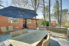 Une terrasse en bois avec une table et des chaises, un parasol bleu et, au fond, un bâtiment en briques.
