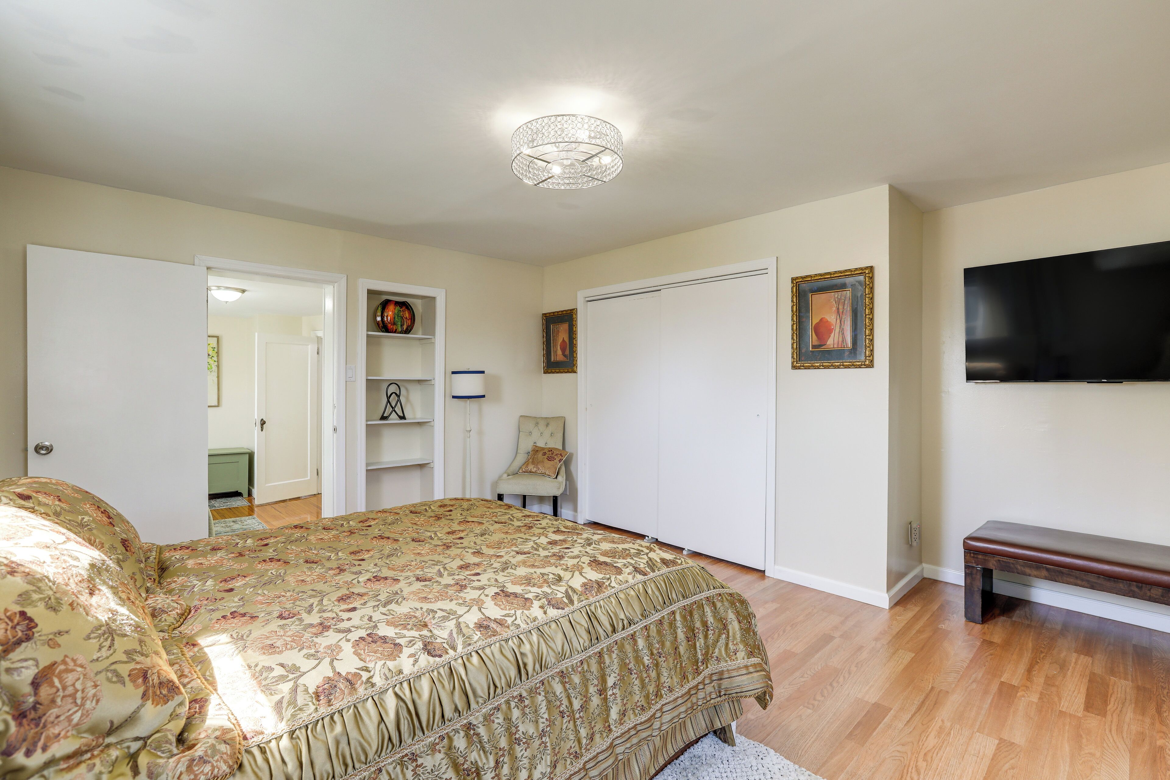 A bedroom with a bed, a TV, a bench, a door, and a ceiling light.