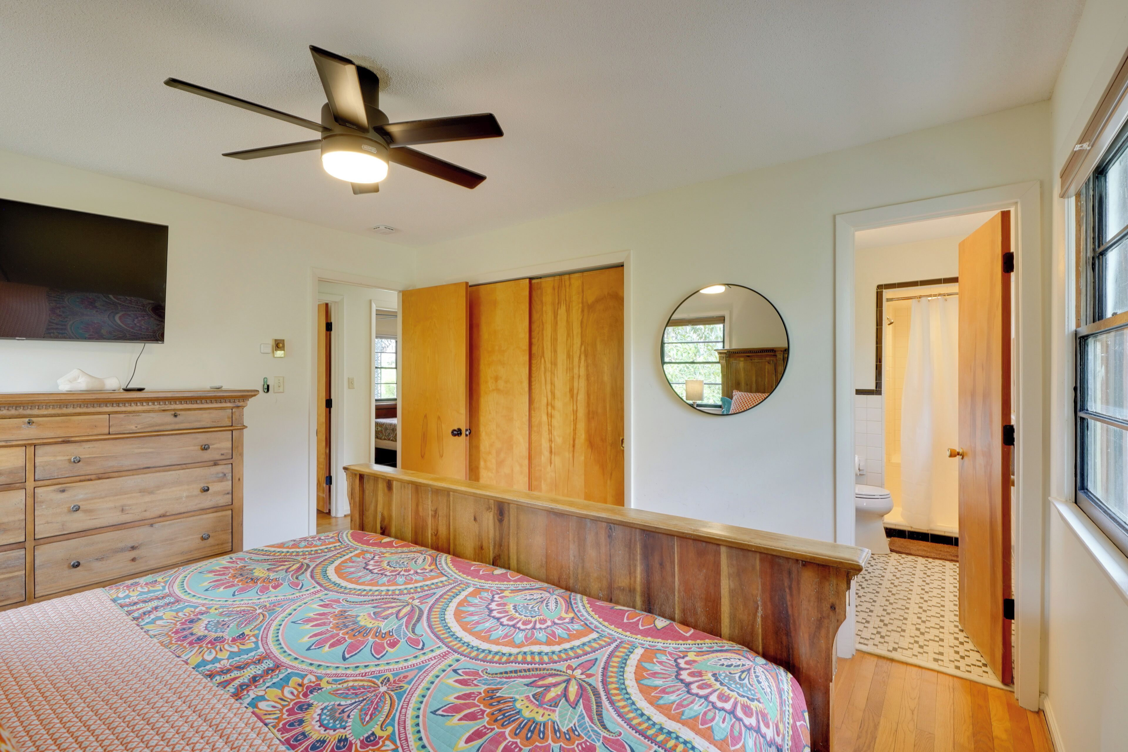 A bedroom with a bed, a ceiling fan, a dresser, a mirror, and a view of the bathroom.