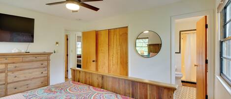 A bedroom with a bed, a ceiling fan, a dresser, a mirror, and a view of the bathroom.
