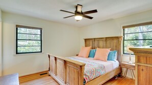 Un dormitorio con una cama de madera, un ventilador de techo, una mesita de noche y una ventana con vistas a árboles.