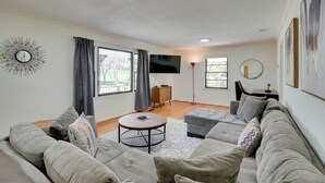 Una sala de estar moderna con un sofá gris, una mesa de centro redonda y un televisor de pantalla plana montado en la pared.