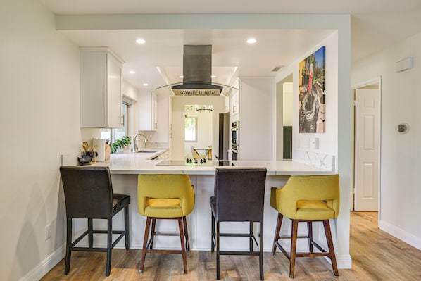 A modern kitchen with a central island, bar stools, and a painting on the wall.