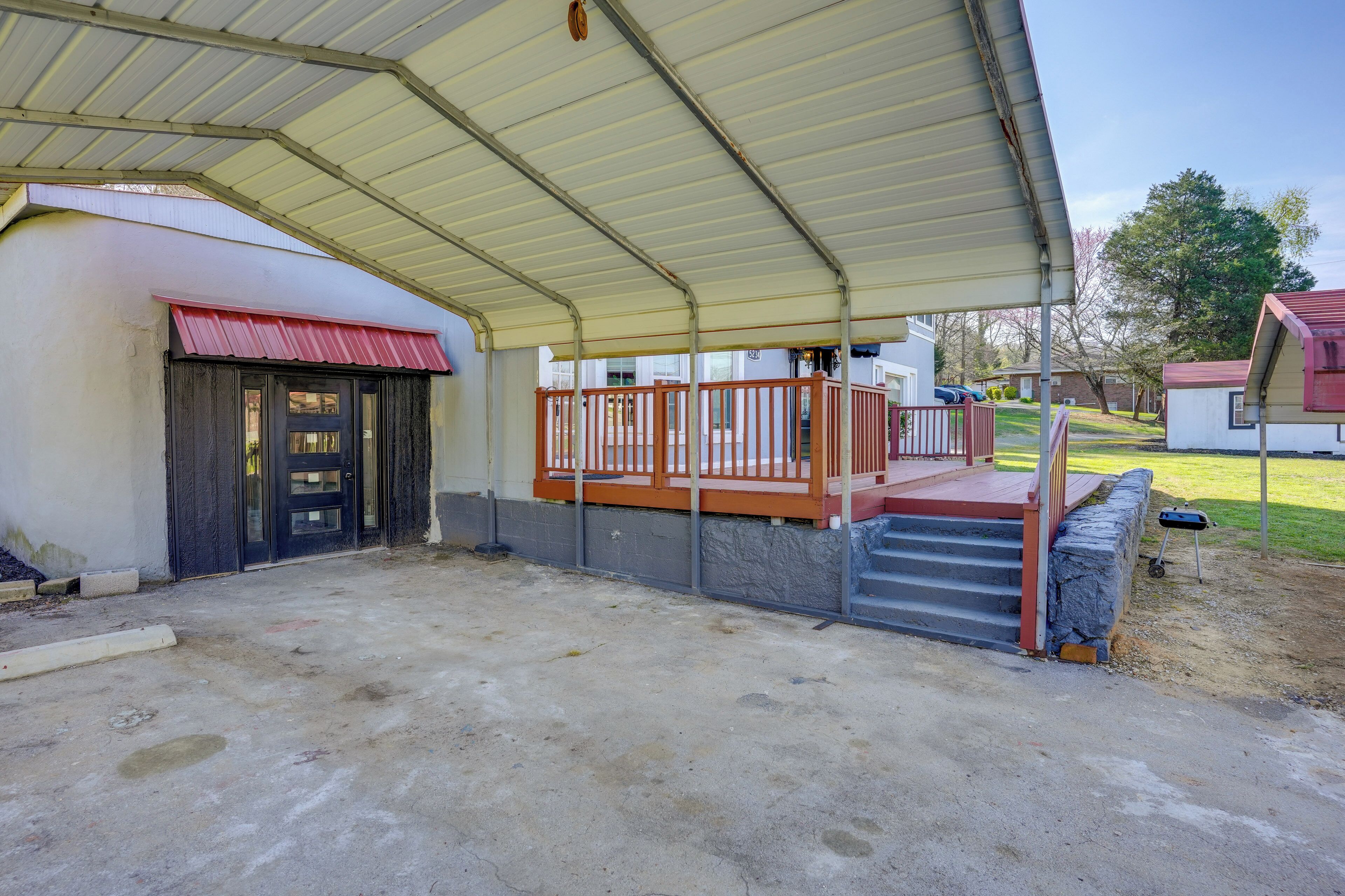 A covered outdoor area with a concrete floor, a wooden deck with a railing, and a stone wall.