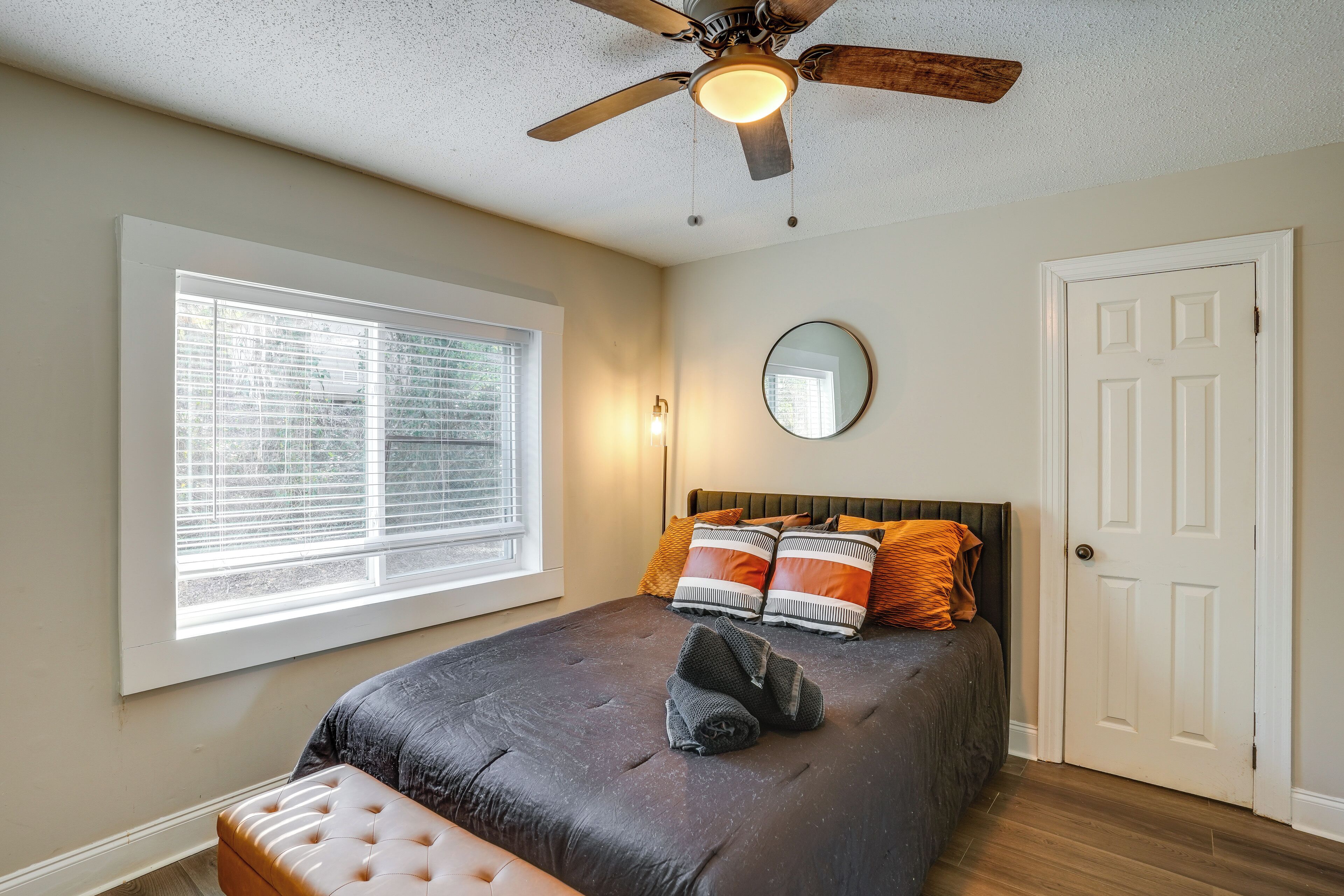A bedroom with a bed, a ceiling fan, a window, a door, and a bedside table.