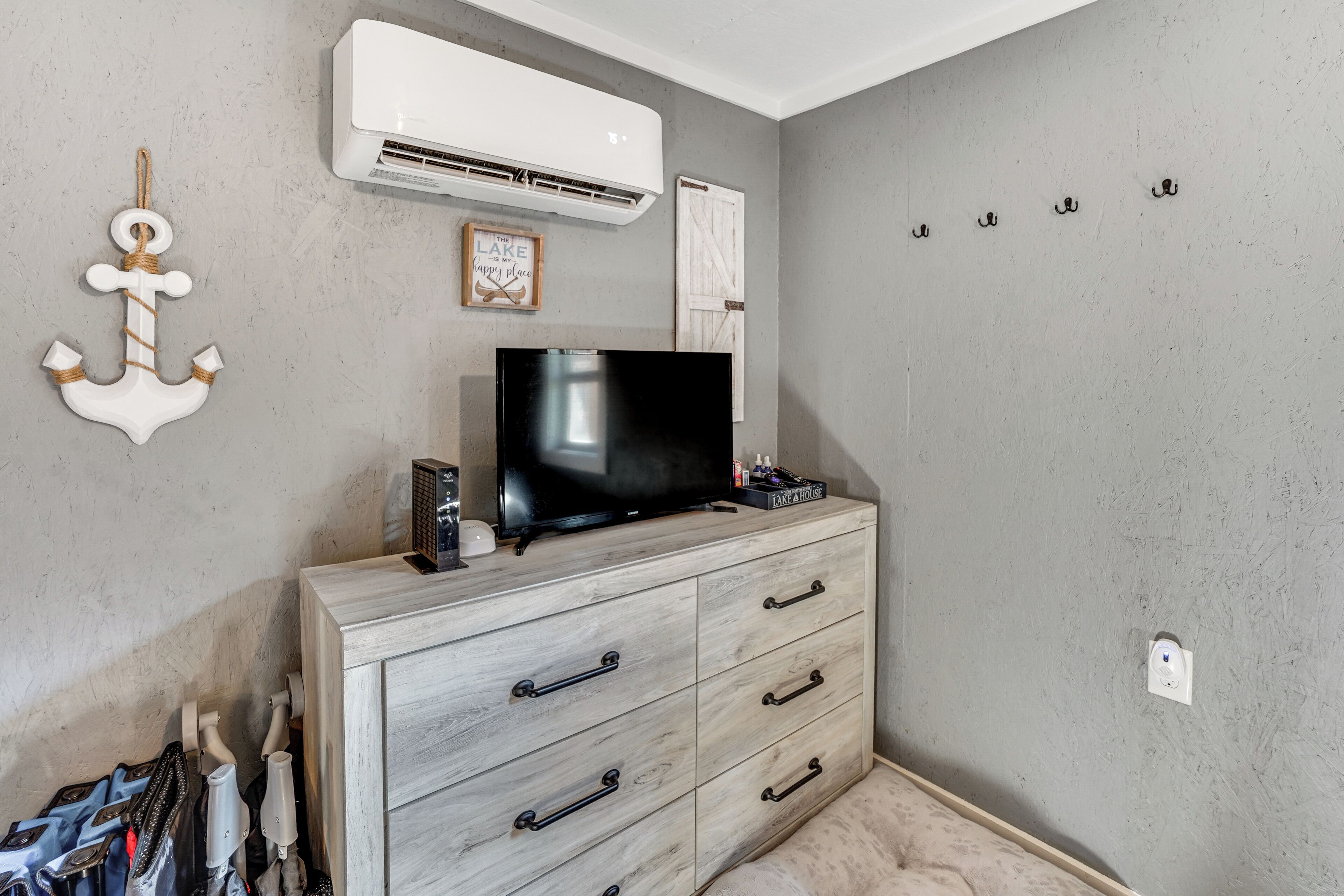 Una habitación con televisión sobre un mueble de madera, aire acondicionado instalado en la pared y un perchero con ganchos.