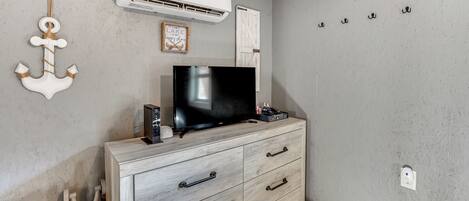 Una habitación con televisión sobre un mueble de madera, aire acondicionado instalado en la pared y un perchero con ganchos.