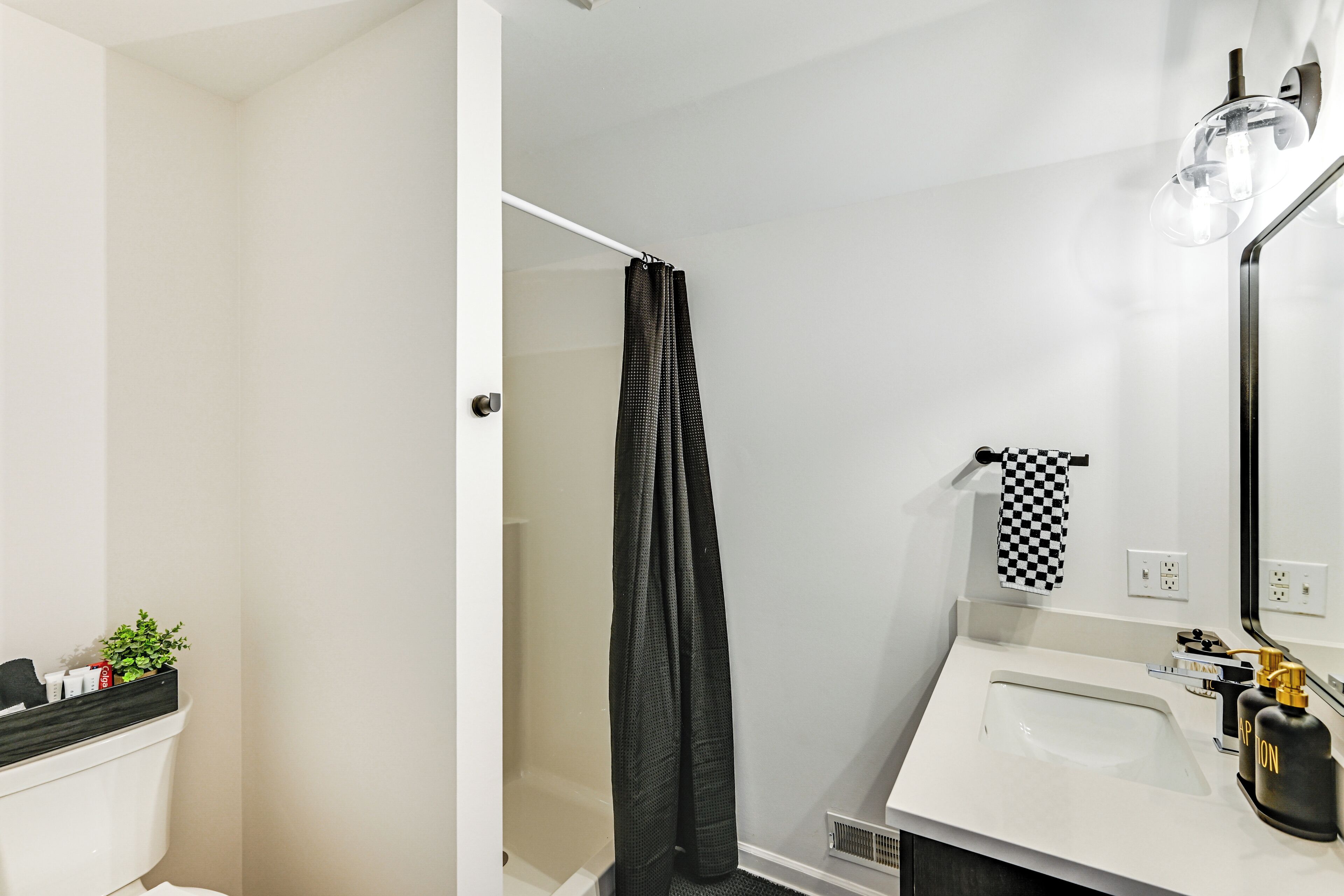 A bathroom with a white sink, a mirror, a black towel, and a shower curtain.