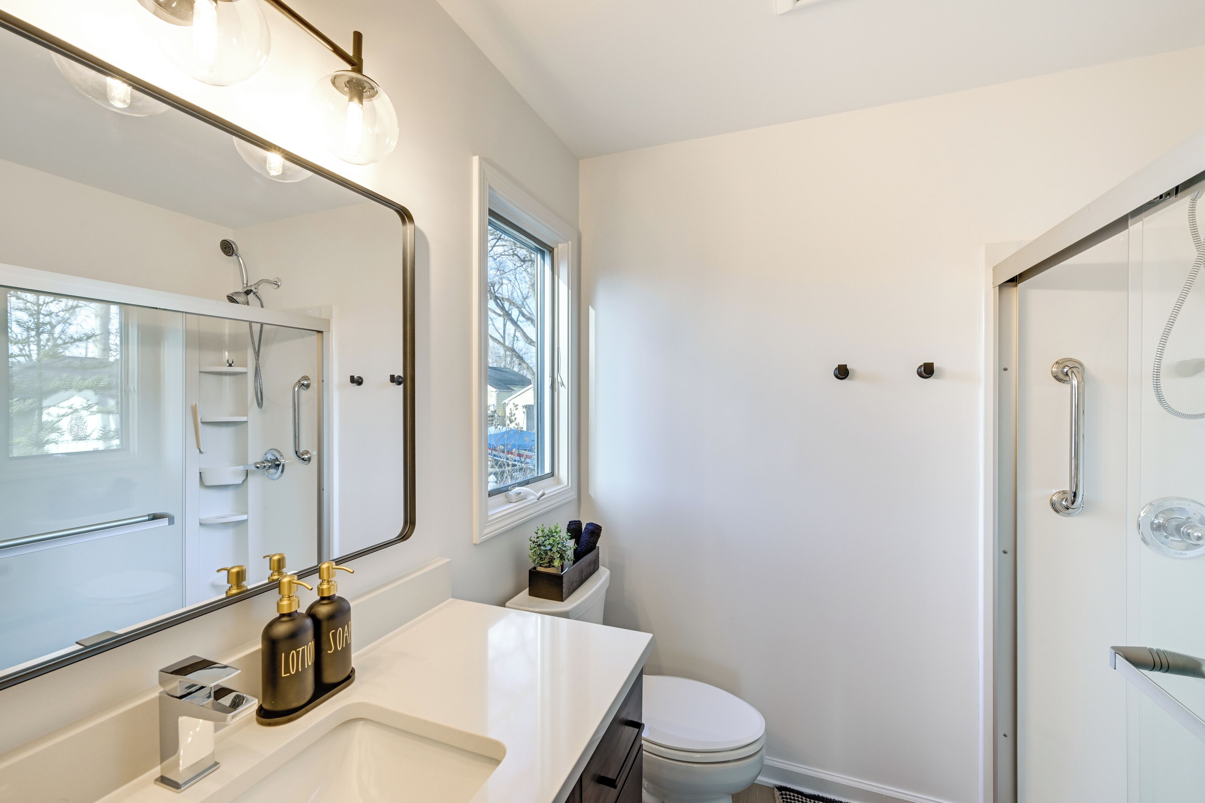 Un baño moderno con un espejo grande, lavamanos blanco y ducha.