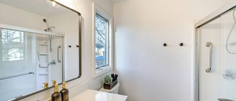 Un baño moderno con un espejo grande, lavamanos blanco y ducha.
