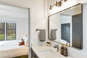 A modern bathroom with a large mirror, a white sink, and a bed with a view of the outdoors.