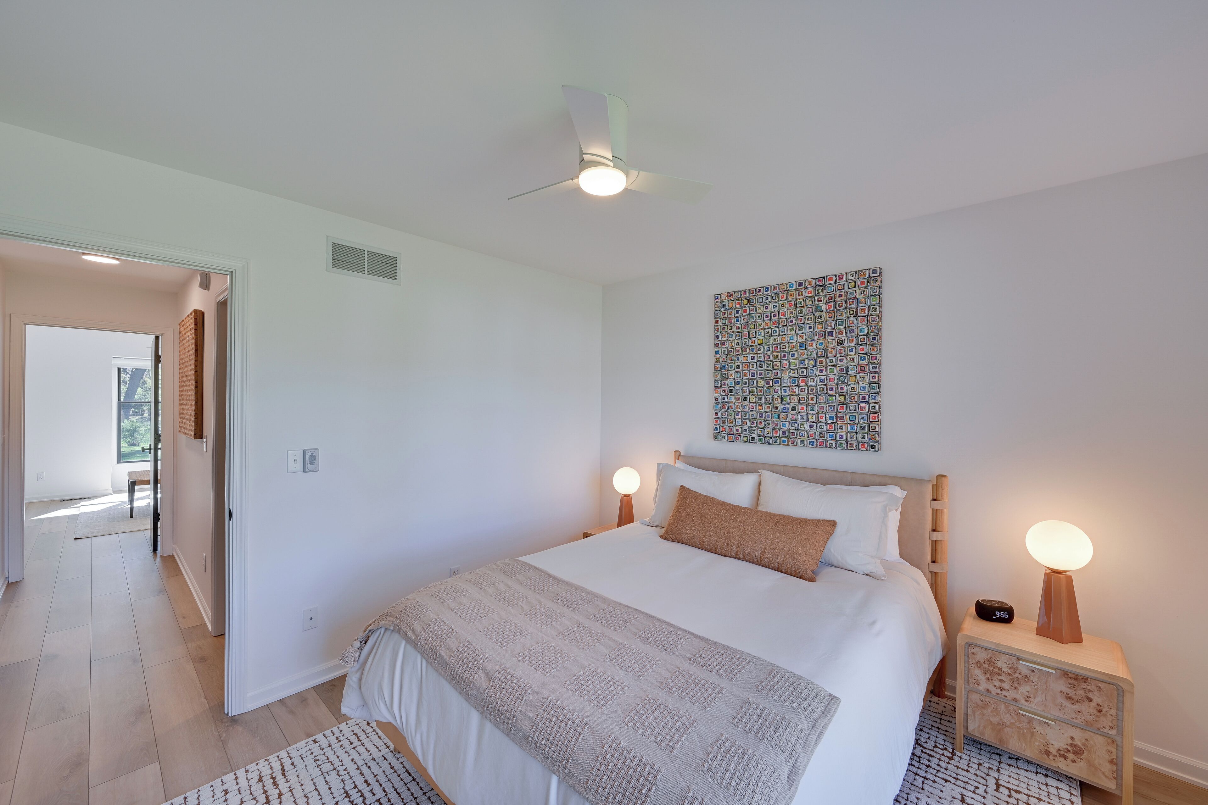 A bedroom with a bed, bedside lamps, a ceiling fan, and a wall art piece.