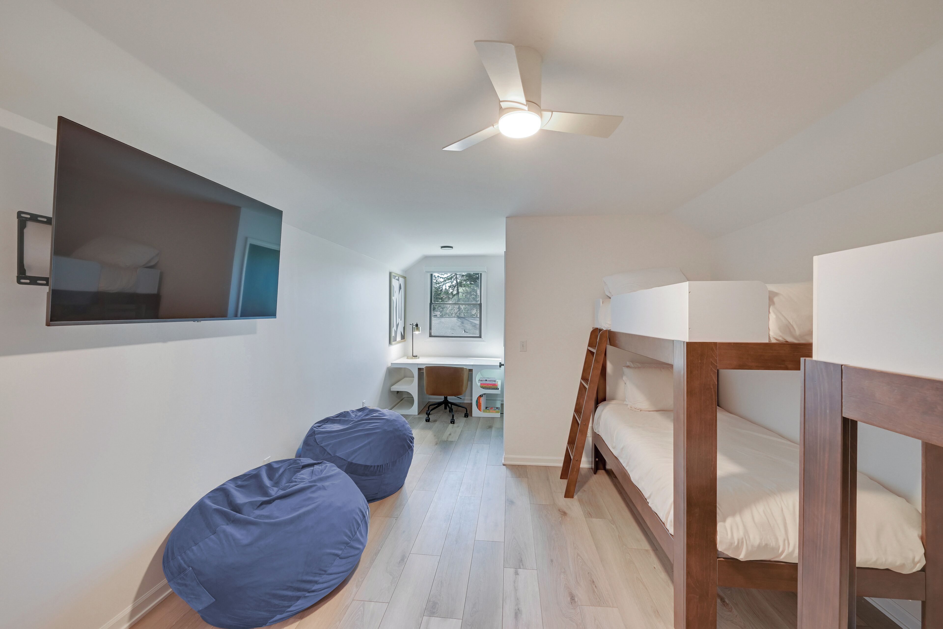 Una habitación con literas, un escritorio, una silla y un ventilador de techo.