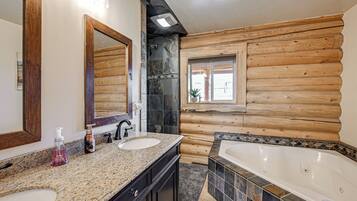 A bathroom with a wooden log wall, a large mirror, two sinks, a bathtub, and a window with a view.