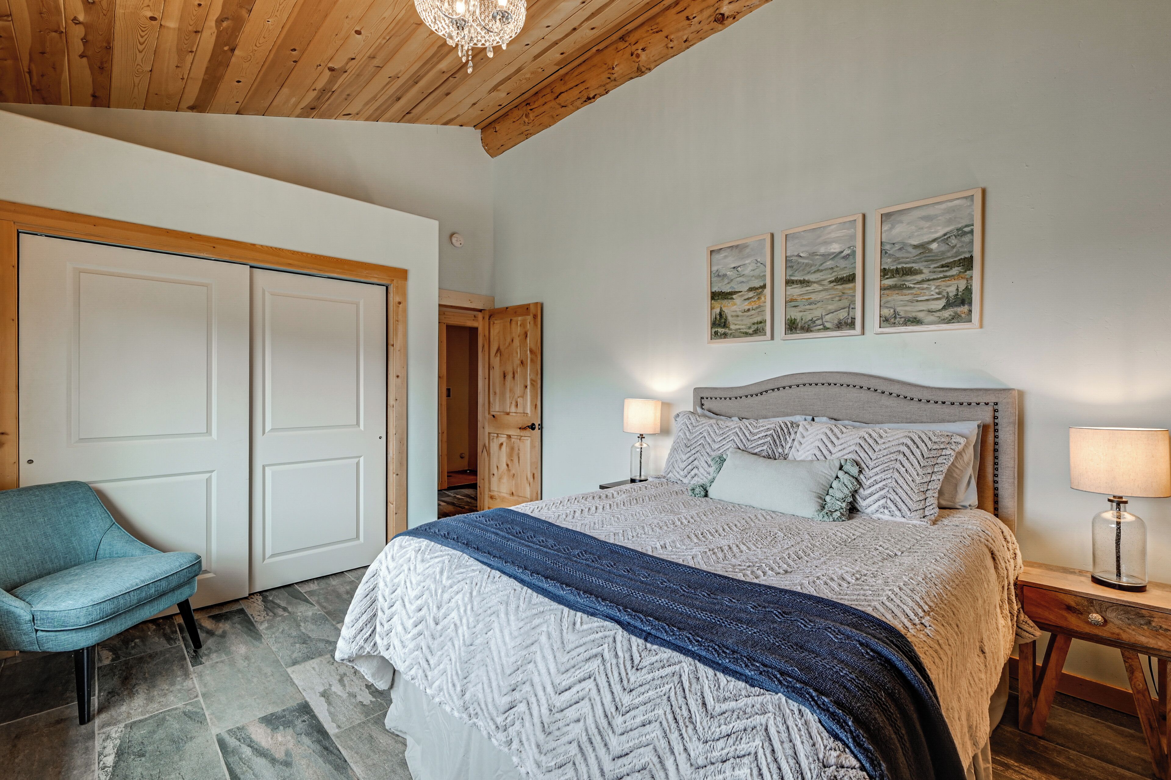 A bedroom with a bed, two bedside lamps, a nightstand, a chair, and two doors.