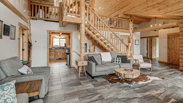 A spacious living area with a wooden staircase, a sofa, a coffee table, and a rug. - Group Retreat in the Bitterroot Valley w/ Hot Tub (Victor)