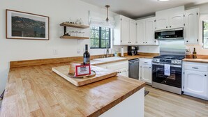 Una cocina con armarios blancos, encimera de madera, horno de acero inoxidable y ventana con vistas.