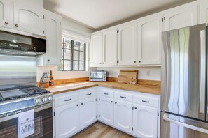 A kitchen with white cabinets, a stainless steel refrigerator, a built-in oven, and a window with a view.