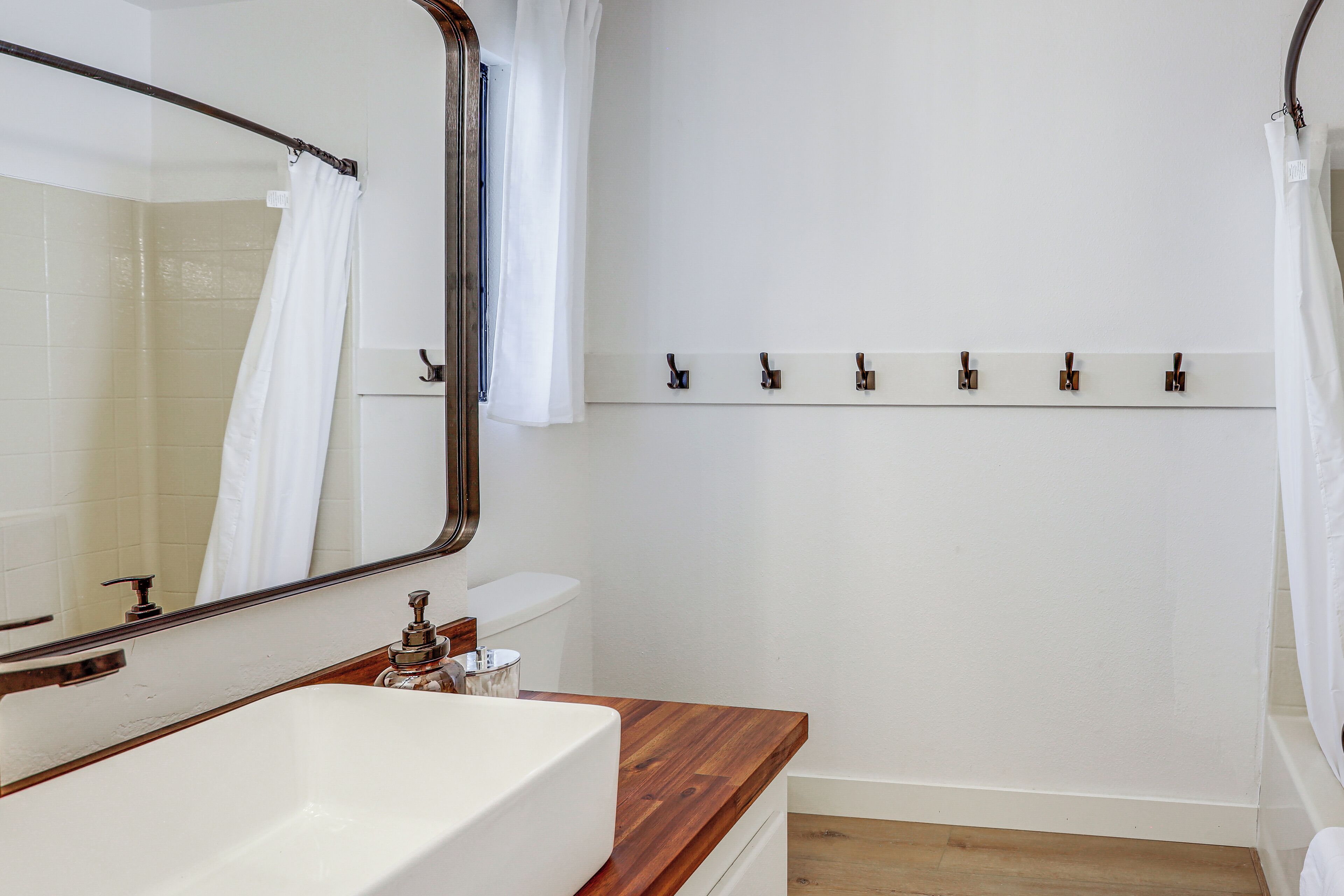 Une salle de bain avec un plan de toilette en bois, un lavabo blanc, un miroir, un rideau de douche et un porte-serviettes.