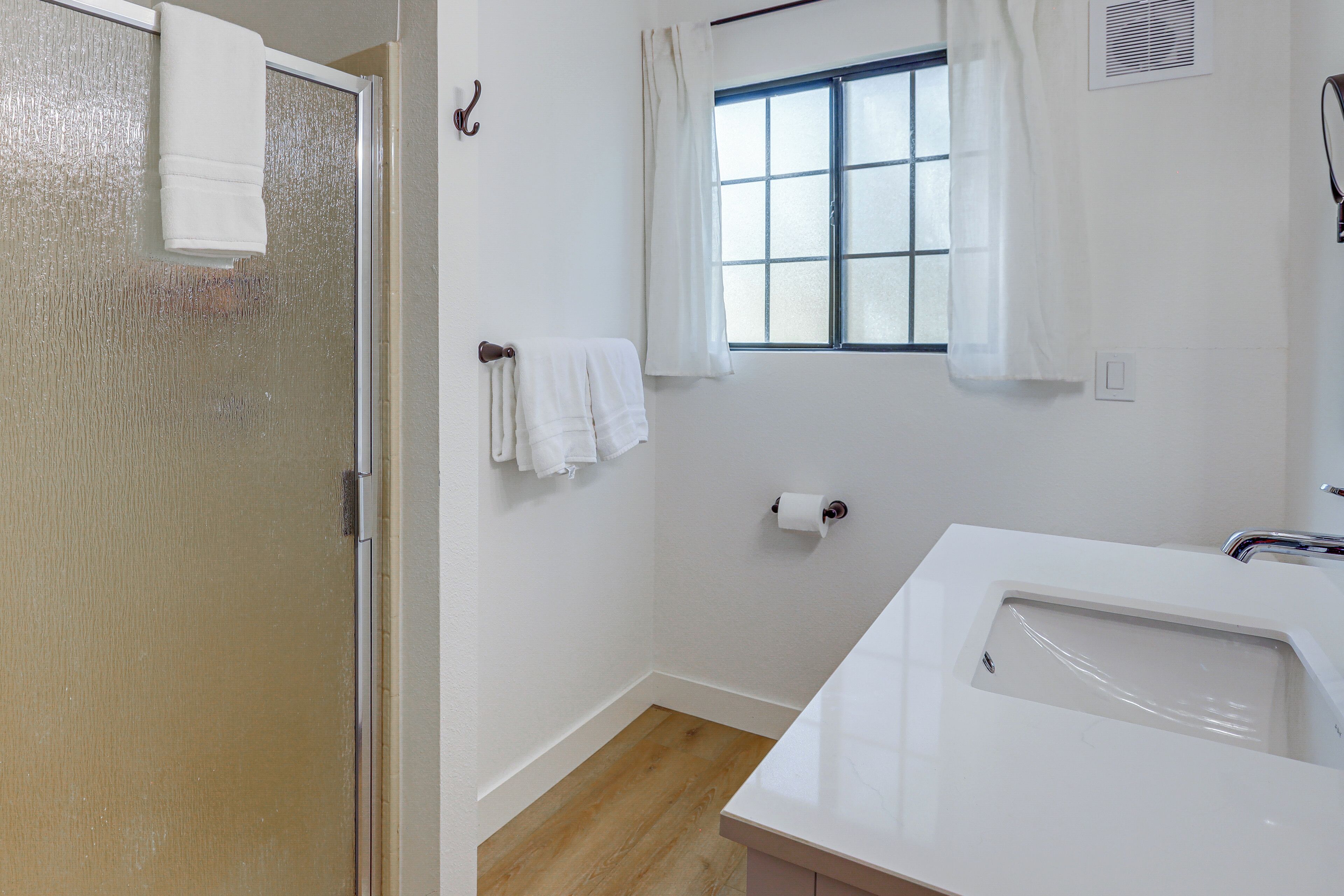 Un baño con ducha, lavamanos, ventana con cortinas y retrete.