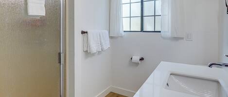 Un baño con ducha, lavamanos, ventana con cortinas y retrete.