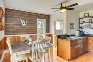 A dining area with a wooden wall, a ceiling fan, and a kitchen with wooden cabinets and a black countertop. - Half-mi to Dtwn Wendell! 60s Farmhouse w/ Fire Pit (Wendell)