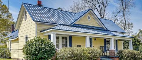 A two-story house with a blue metal roof, a front porch with steps, and a brick chimney.