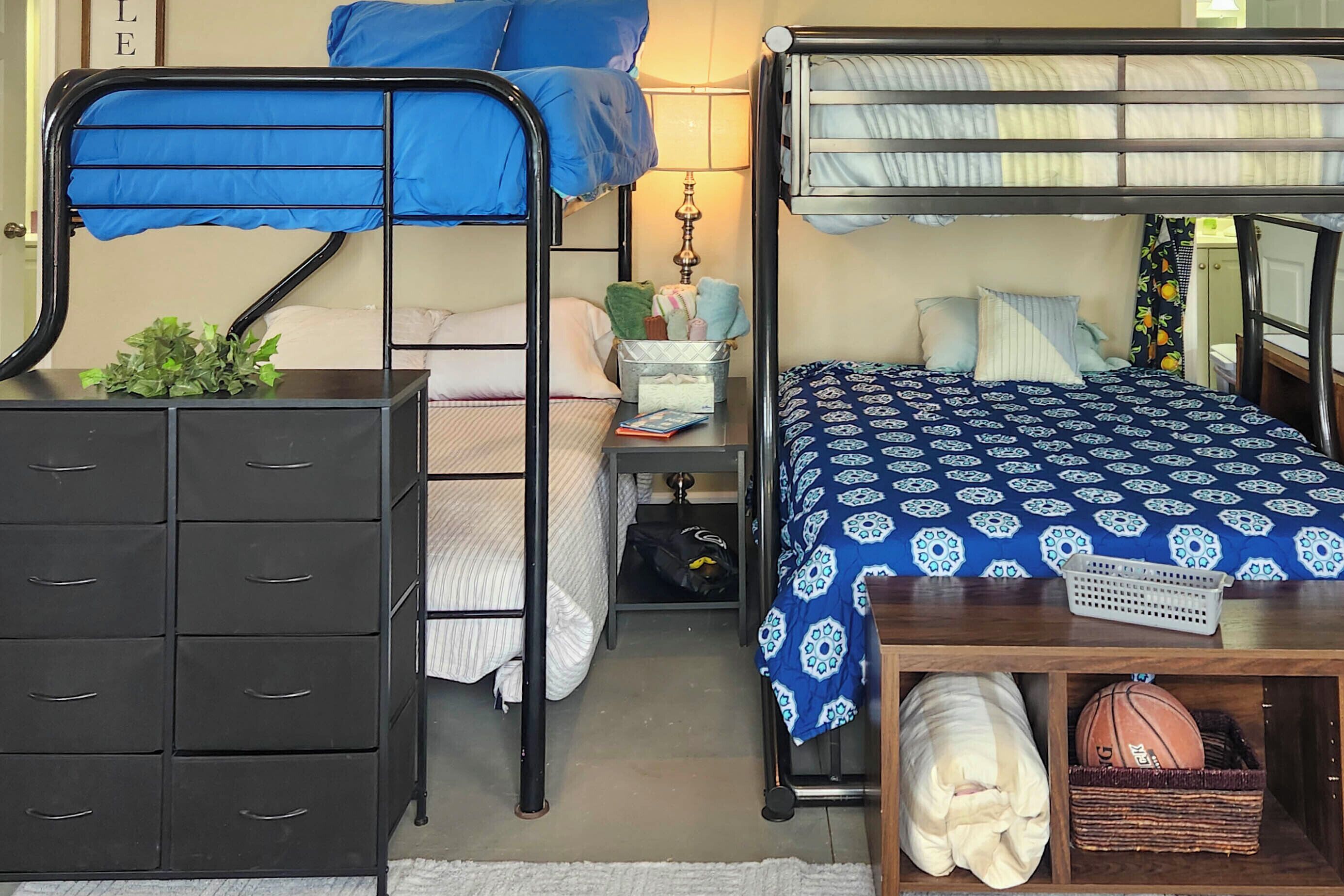 A bunk bed room with a metal dresser, a bedside table with a lamp, and a basket with a basketball.