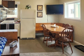 A compact kitchen with a refrigerator, microwave, and stove, a dining table with chairs, a television mounted on the wall, and a window providing natural light. - Ozark Mountain Launchpad! Cabin w/ Fishing On-site (Richland)
