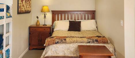 A bedroom with a bed, bedside table, lamp, and a small wooden stool.