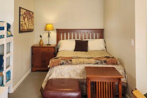 Un dormitorio con cama, mesita de noche, lámpara y un taburete de madera.