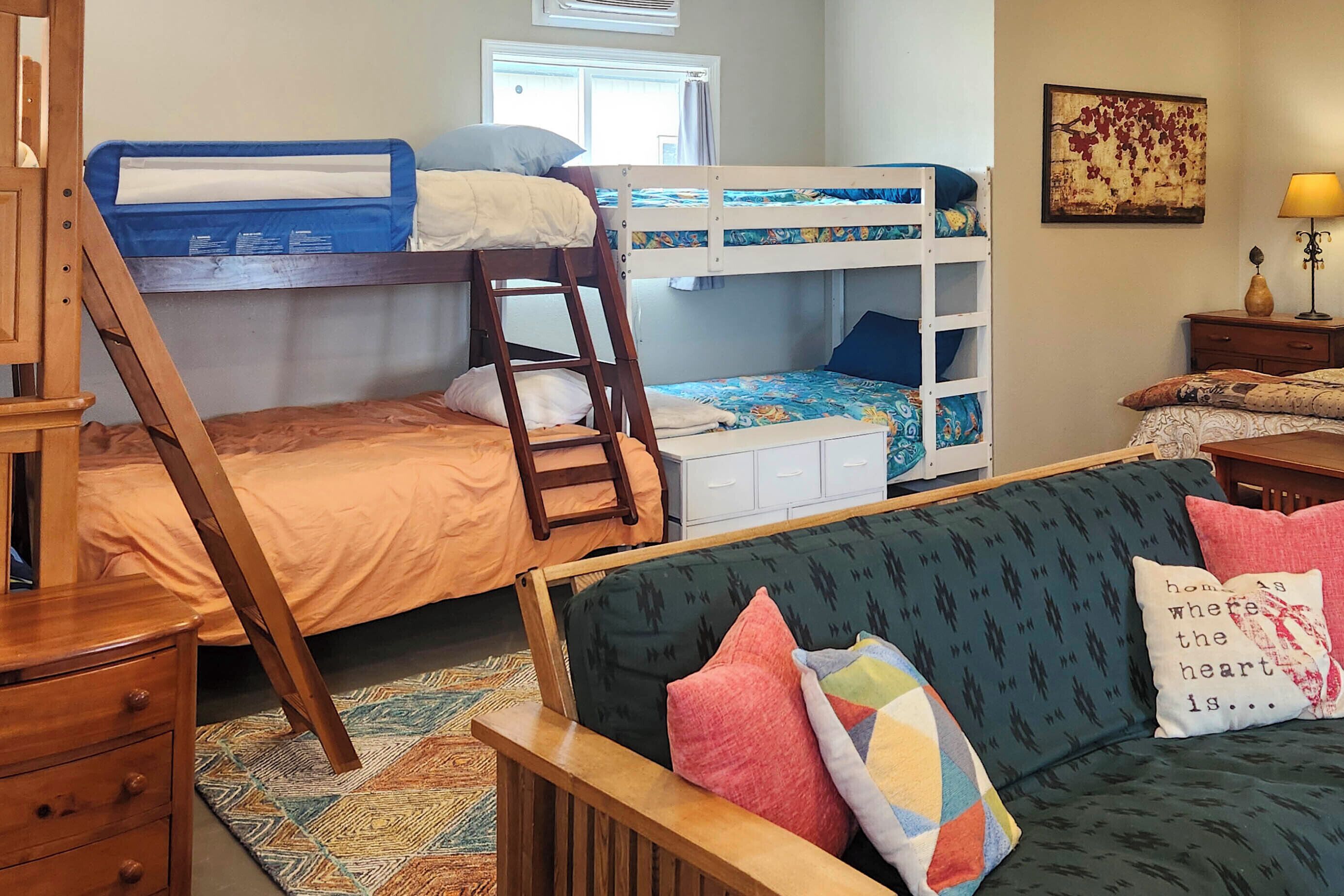 A bunk bed room with a ladder, a couch, a wooden dresser, and a window with curtains.