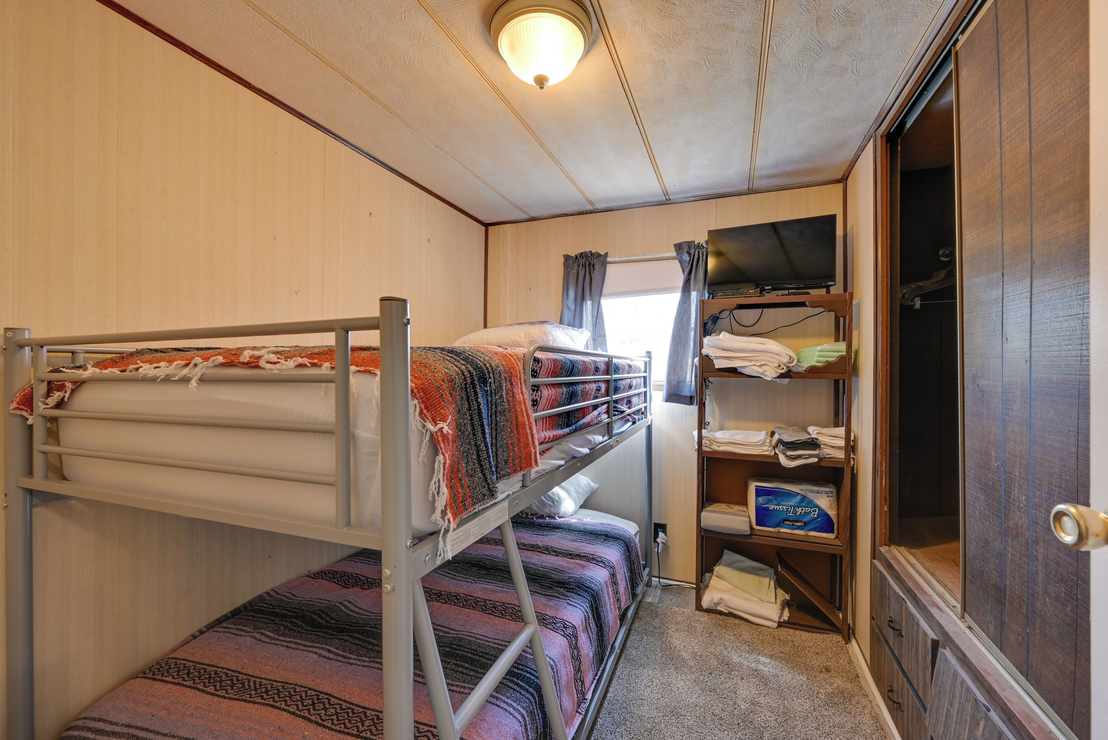 A bunk bed with a patterned blanket, a shelf with folded clothes, and a television.