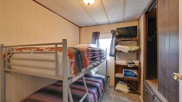 A bunk bed with a patterned blanket, a shelf with folded clothes, and a television.
