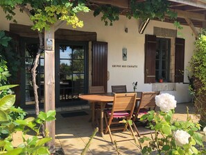 A rustic outdoor seating area with a wooden table and chairs, a pergola with climbing plants, and a wall-mounted sign. - Comfortable gîte for 4 people with swimming pool, large garden - 15 km from the sea (Chenac-Saint-Seurin-d'Uzet)