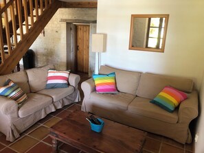 A living room with two beige sofas, colorful striped pillows, a wooden coffee table, and a wooden staircase. - Comfortable gîte for 4 people with swimming pool, large garden - 15 km from the sea (Chenac-Saint-Seurin-d'Uzet)