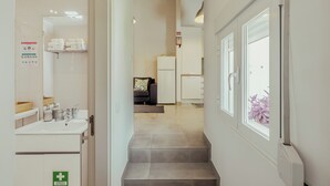 Ein Flur mit Bad auf der linken Seite, einer Couch und einem Kühlschrank in der Mitte und einem Fenster rechts.